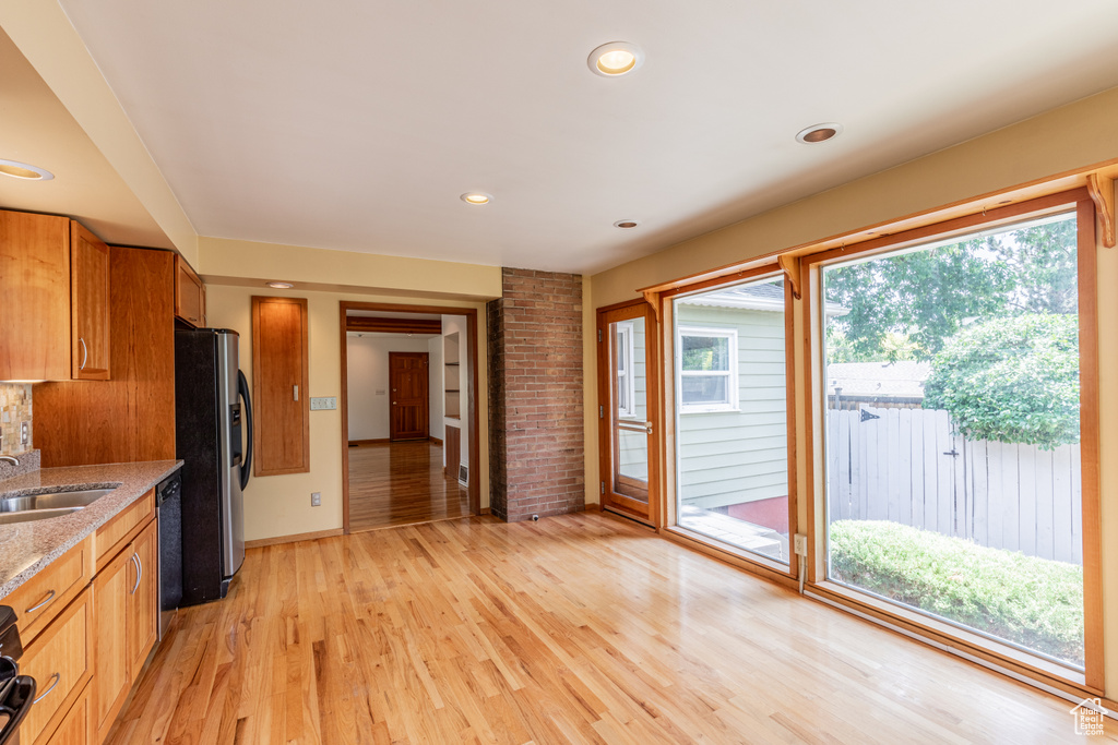 Kitchen featuring stainless steel fridge with ice dispenser, light hardwood / wood-style floors, dishwashing machine, sink, and brick wall