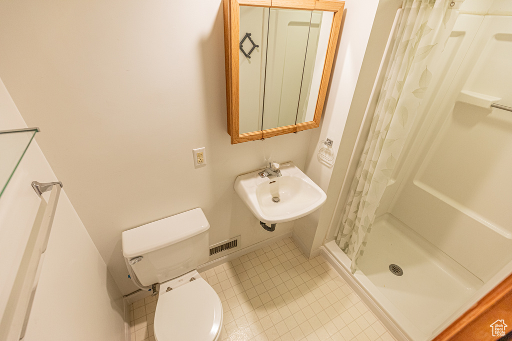 Bathroom with sink, curtained shower, toilet, and tile patterned flooring