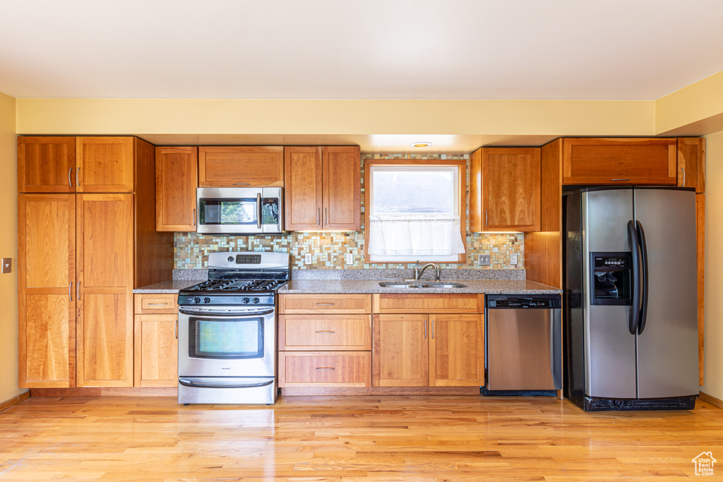 Kitchen featuring decorative backsplash, light hardwood / wood-style flooring, stone countertops, stainless steel appliances, and sink