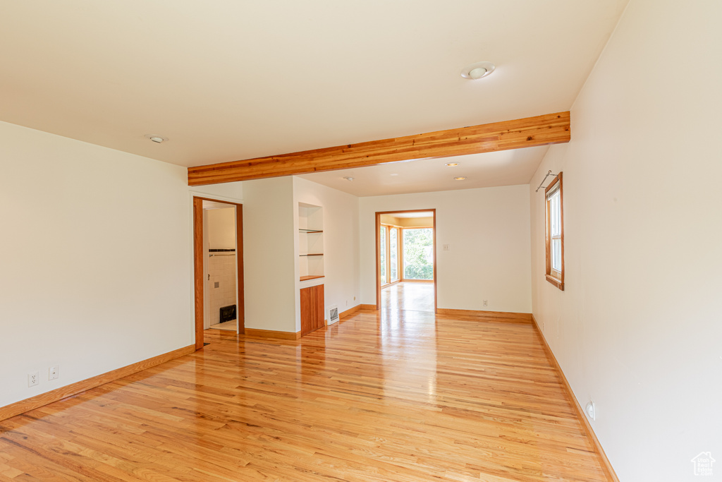 Unfurnished room featuring beamed ceiling, built in features, and light wood-type flooring