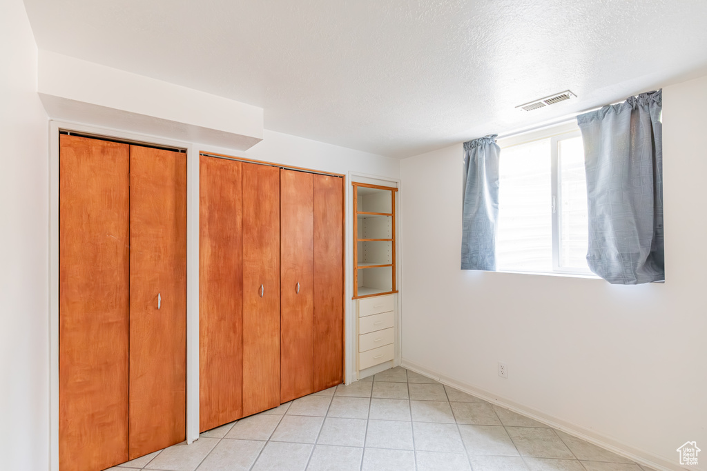 Unfurnished bedroom featuring a textured ceiling, multiple closets, and light tile patterned floors