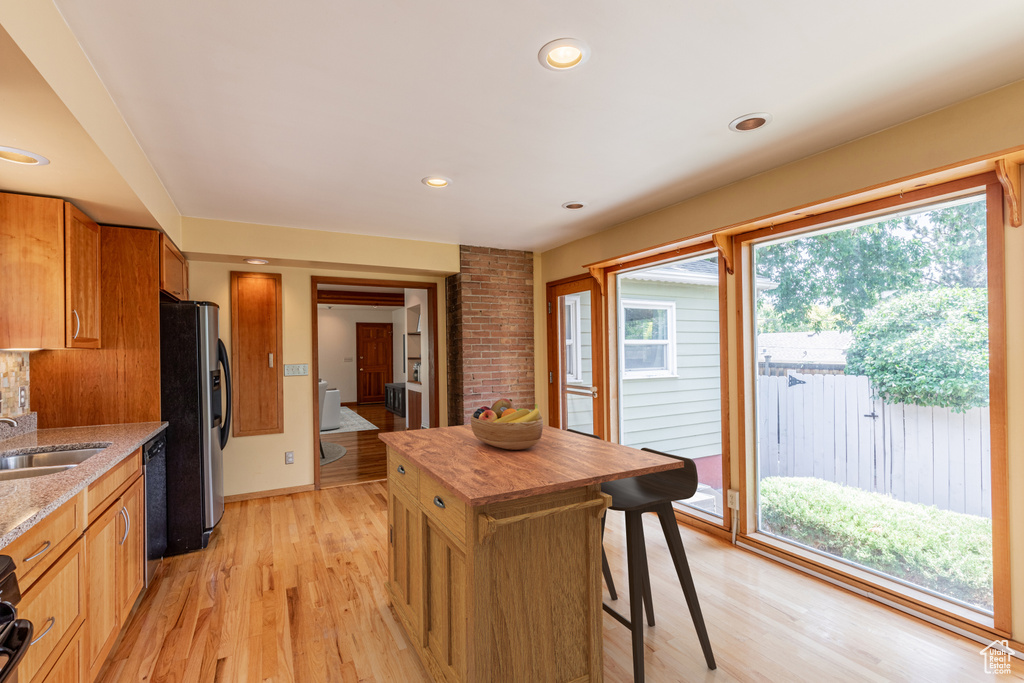 Kitchen with stainless steel fridge with ice dispenser, dishwasher, brick wall, light wood-type flooring, and sink