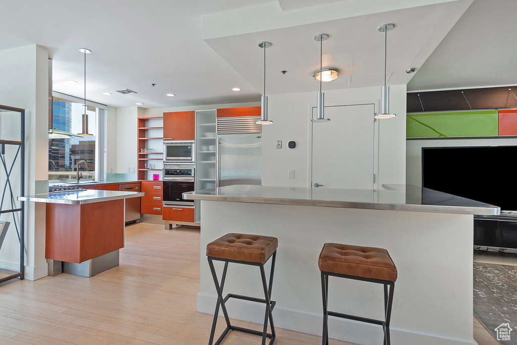 Kitchen with built in appliances, a breakfast bar, pendant lighting, light hardwood / wood-style floors, and a kitchen island