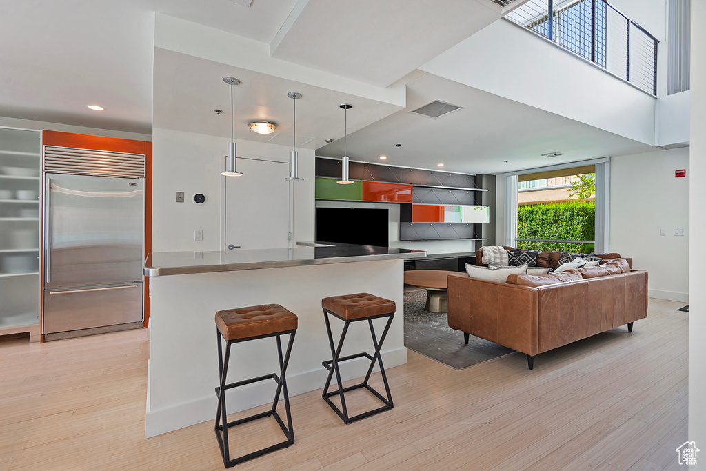 Kitchen featuring light hardwood / wood-style flooring, decorative light fixtures, built in refrigerator, and a breakfast bar