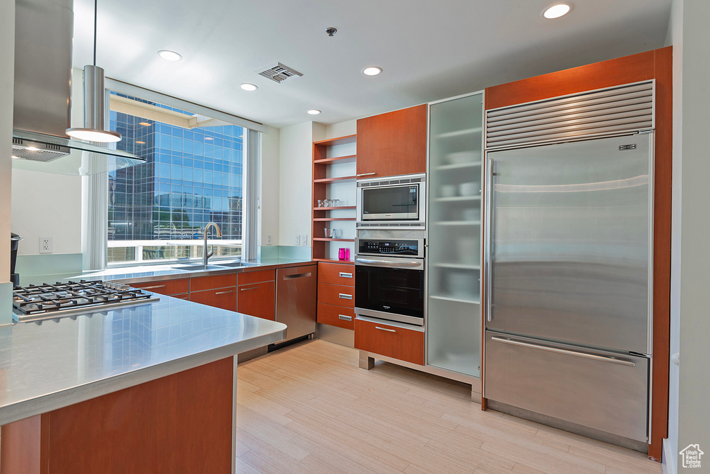 Kitchen featuring built in appliances, light hardwood / wood-style flooring, sink, and stainless steel counters