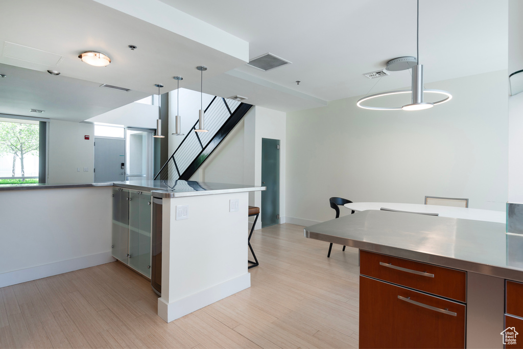 Kitchen featuring hanging light fixtures, a breakfast bar area, stainless steel counters, light hardwood / wood-style floors, and kitchen peninsula