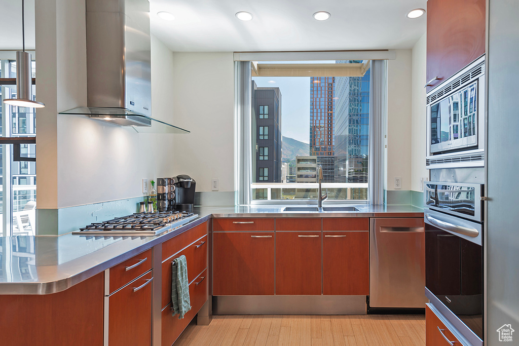 Kitchen with appliances with stainless steel finishes, stainless steel counters, sink, light hardwood / wood-style floors, and wall chimney range hood