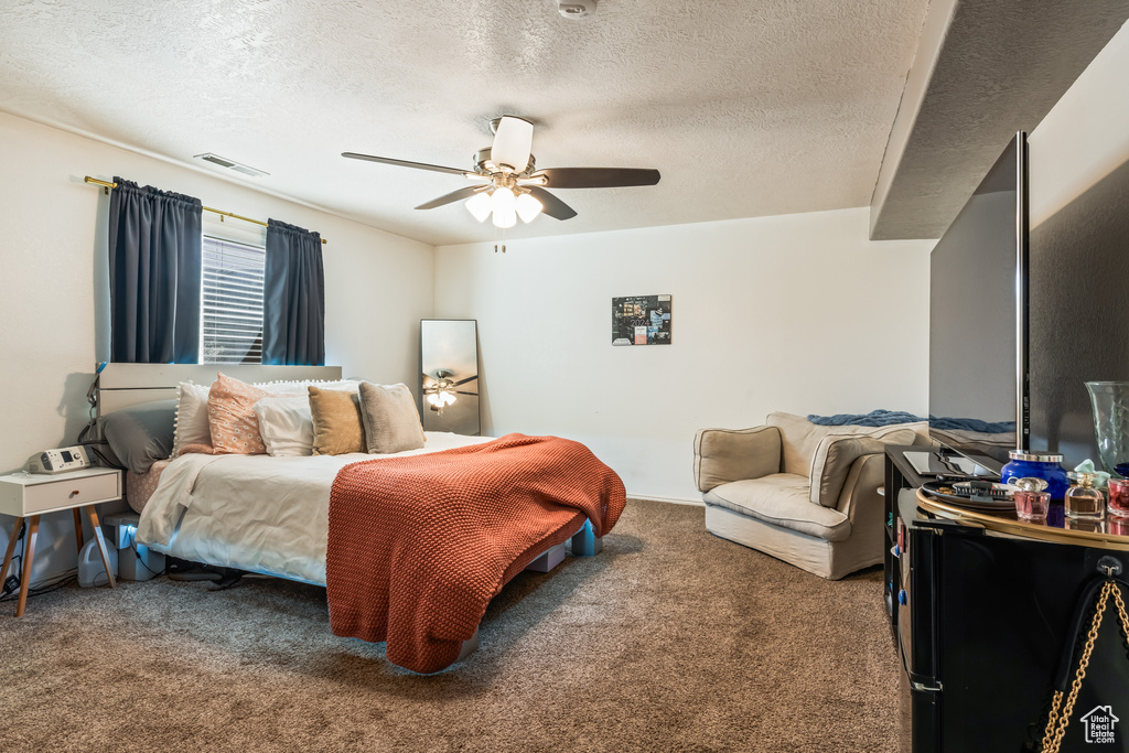 Carpeted bedroom featuring ceiling fan and a textured ceiling