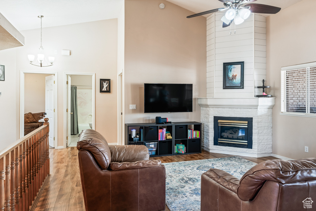 Living room featuring high vaulted ceiling, a fireplace, ceiling fan with notable chandelier, and hardwood / wood-style floors