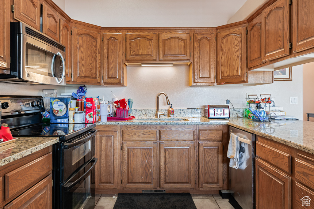 Kitchen with light stone counters, appliances with stainless steel finishes, light tile patterned flooring, and sink