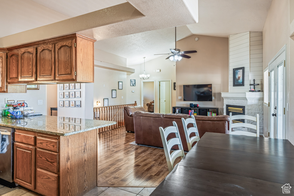 Kitchen featuring light wood-type flooring, ceiling fan with notable chandelier, a textured ceiling, lofted ceiling, and light stone counters