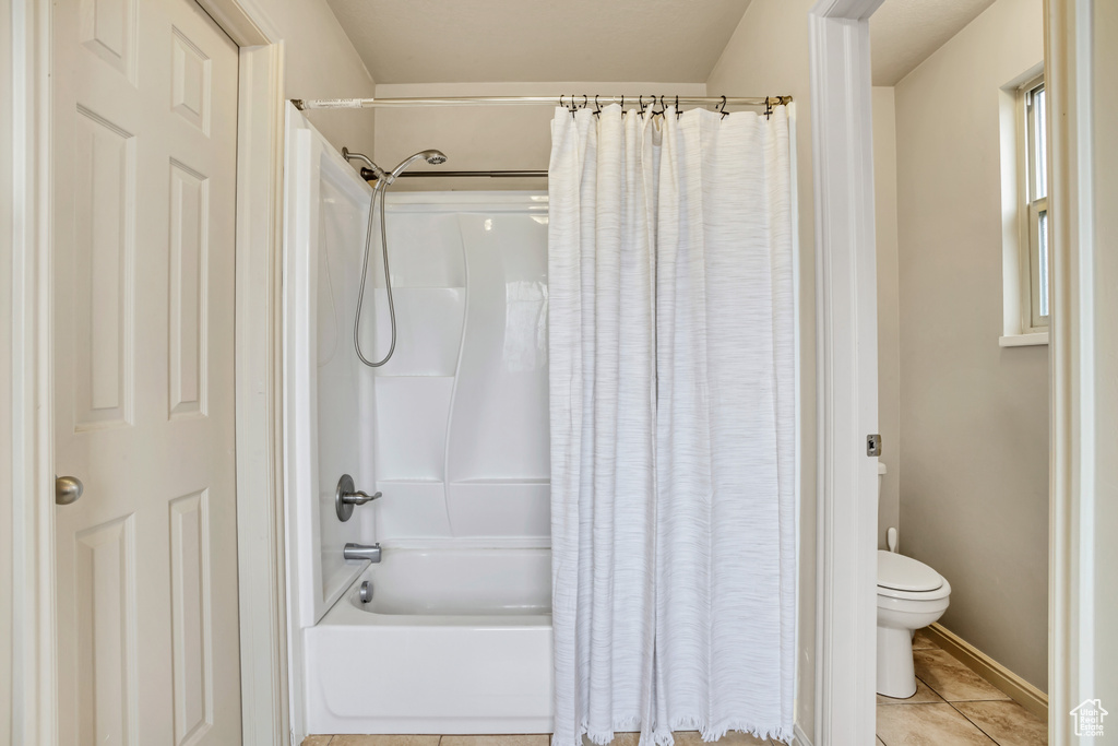 Bathroom with toilet, shower / bath combo with shower curtain, and tile patterned floors