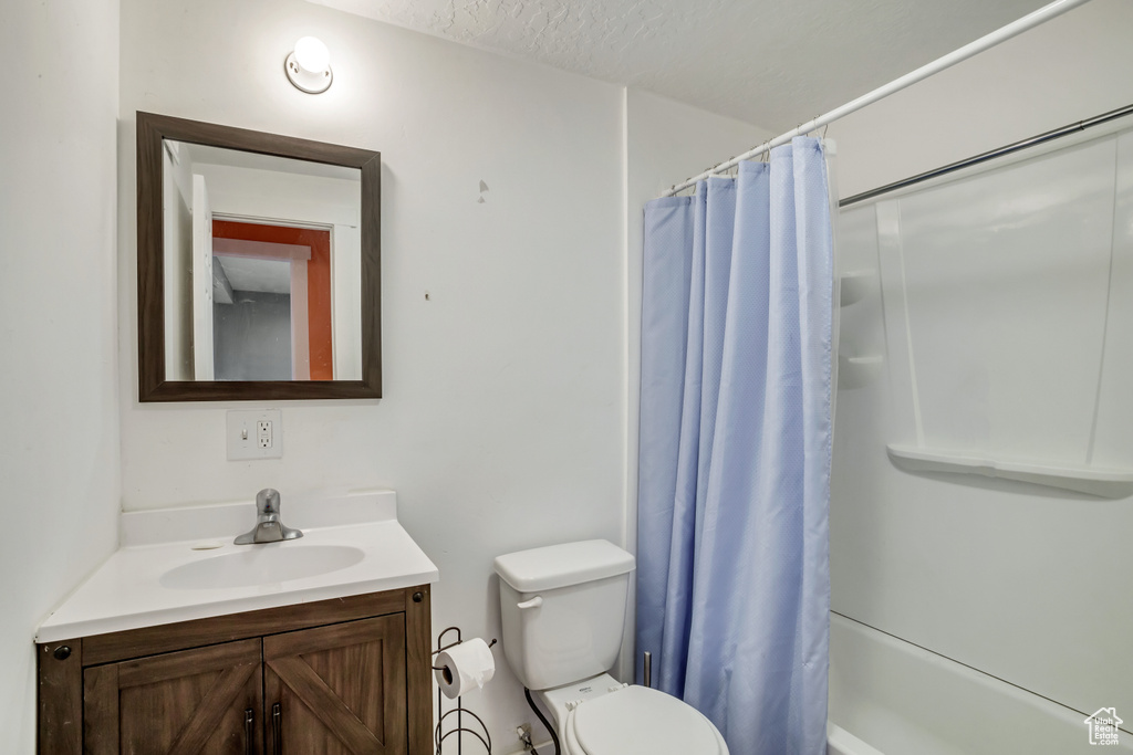 Full bathroom featuring a textured ceiling, toilet, shower / bath combo with shower curtain, and vanity