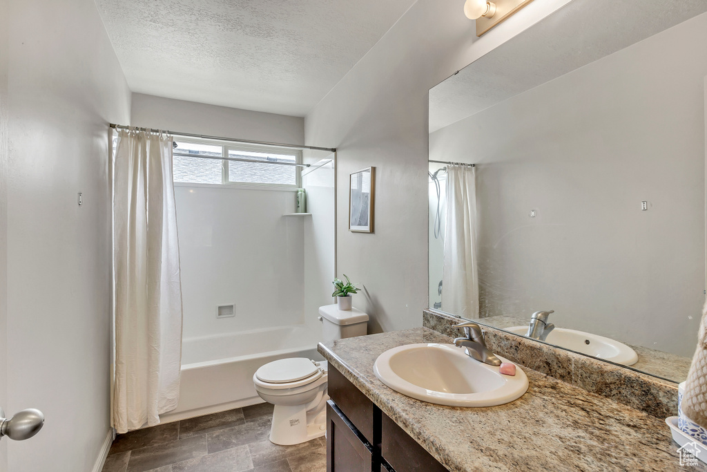 Full bathroom with a textured ceiling, toilet, shower / tub combo, vanity, and tile patterned floors