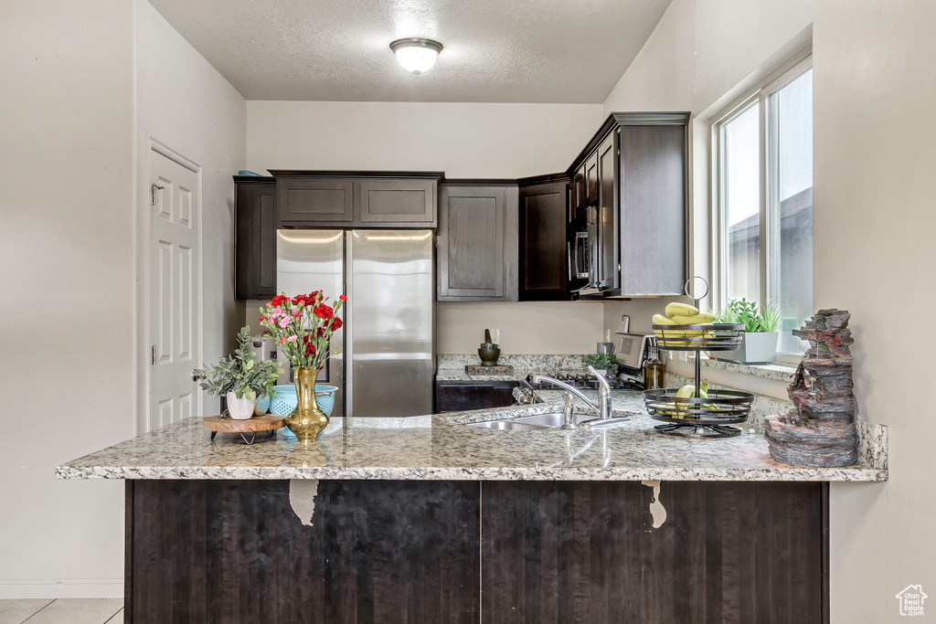 Kitchen featuring kitchen peninsula, stainless steel refrigerator, and light stone countertops