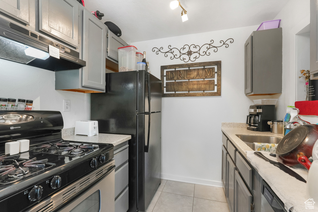 Kitchen featuring range with gas cooktop, black refrigerator, light tile patterned floors, gray cabinetry, and track lighting