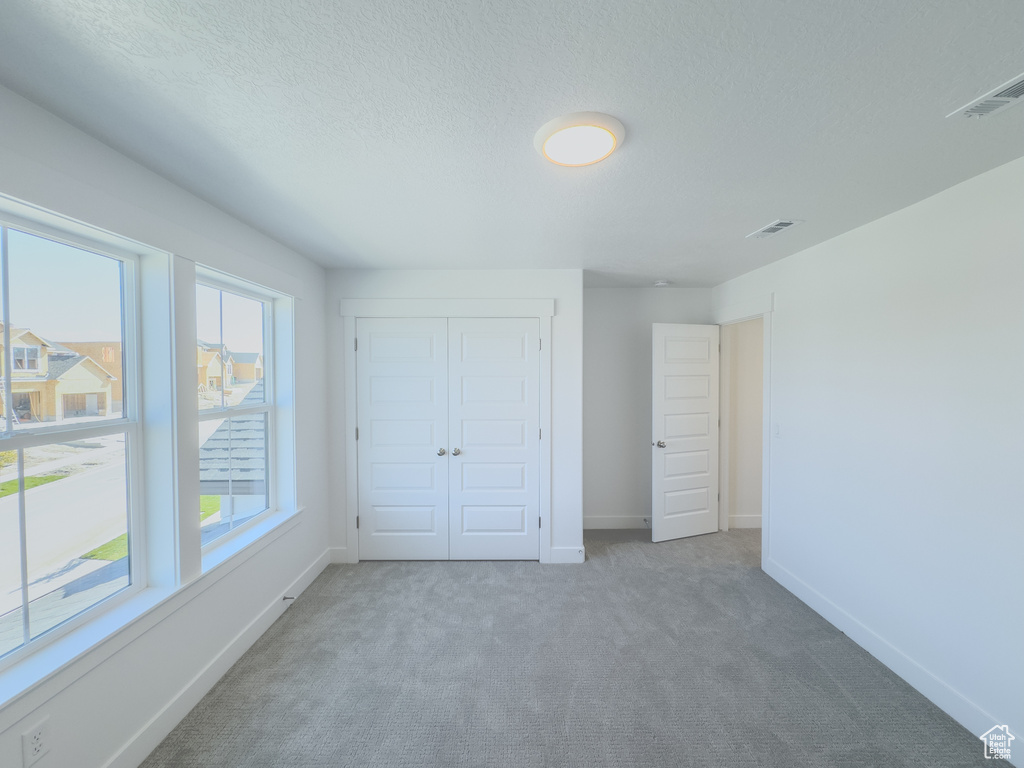 Unfurnished bedroom with light carpet, a textured ceiling, and a closet