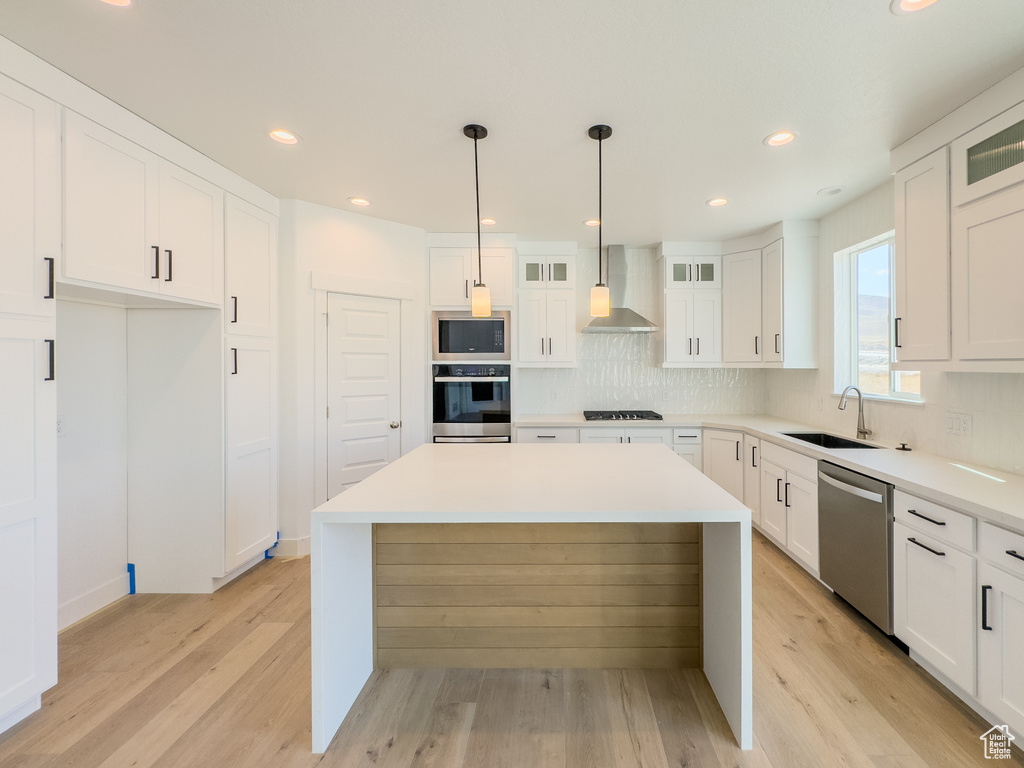 Kitchen with white cabinets, stainless steel appliances, wall chimney range hood, and light hardwood / wood-style flooring