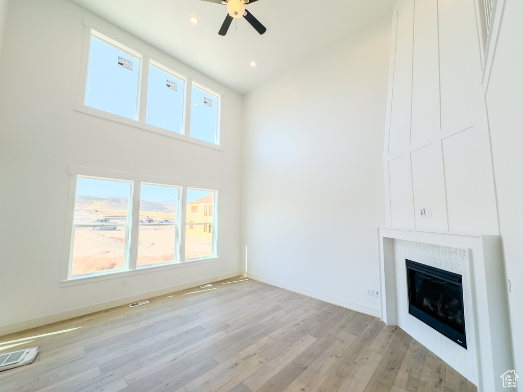 Unfurnished living room featuring a high ceiling, ceiling fan, a wealth of natural light, and light hardwood / wood-style floors