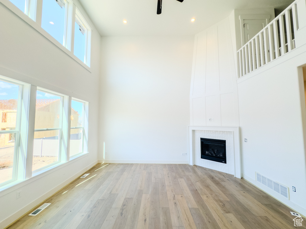 Unfurnished living room featuring plenty of natural light, a high ceiling, light hardwood / wood-style flooring, and ceiling fan