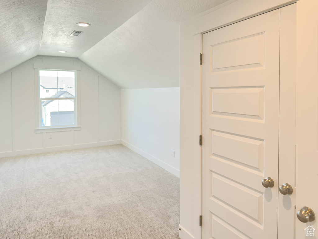 Bonus room with vaulted ceiling, a textured ceiling, and light carpet