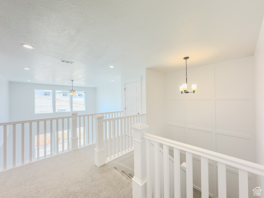 Corridor featuring a notable chandelier, carpet, and a textured ceiling