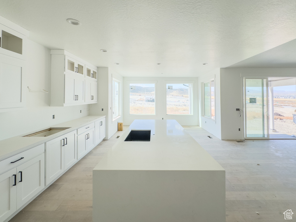 Kitchen featuring white cabinets, a textured ceiling, light hardwood / wood-style floors, and a kitchen island