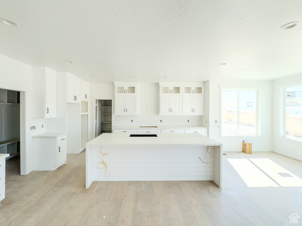 Kitchen featuring light wood-type flooring, a breakfast bar area, white cabinetry, a spacious island, and a textured ceiling