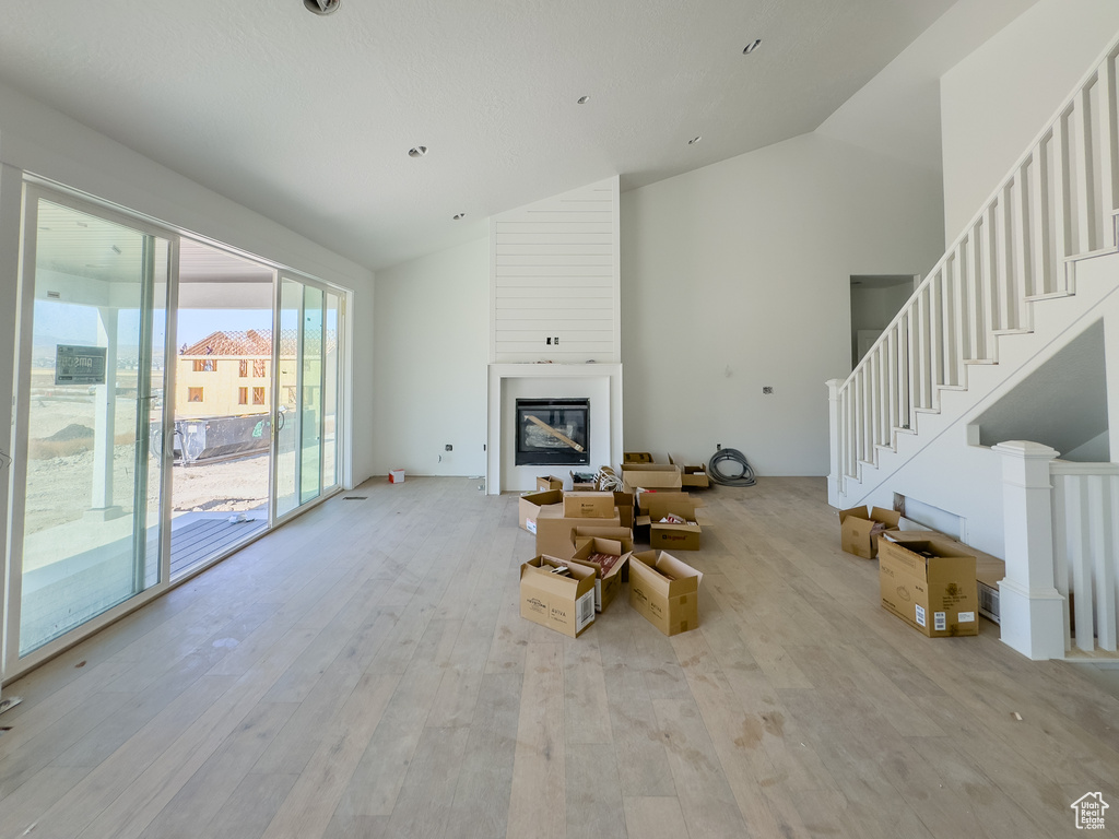 Unfurnished living room featuring a fireplace, high vaulted ceiling, and light wood-type flooring