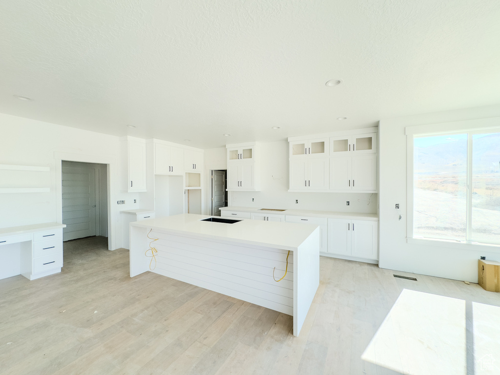 Kitchen featuring light hardwood / wood-style floors, a kitchen breakfast bar, white cabinets, a large island, and a textured ceiling