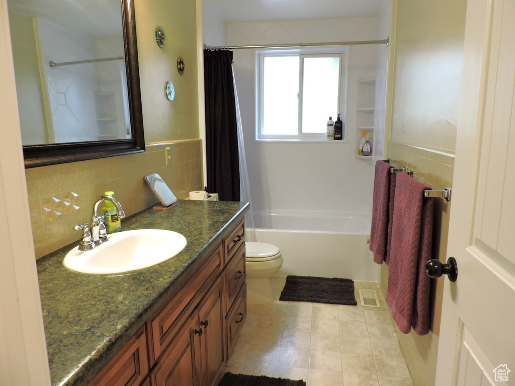 Full bathroom with tasteful backsplash, toilet, tile patterned floors, shower / bath combination with curtain, and vanity