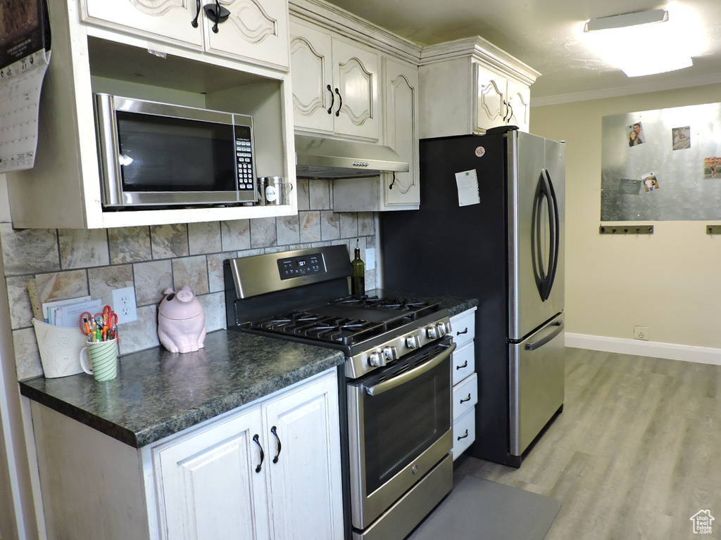 Kitchen featuring stainless steel appliances, decorative backsplash, ornamental molding, white cabinetry, and light hardwood / wood-style floors