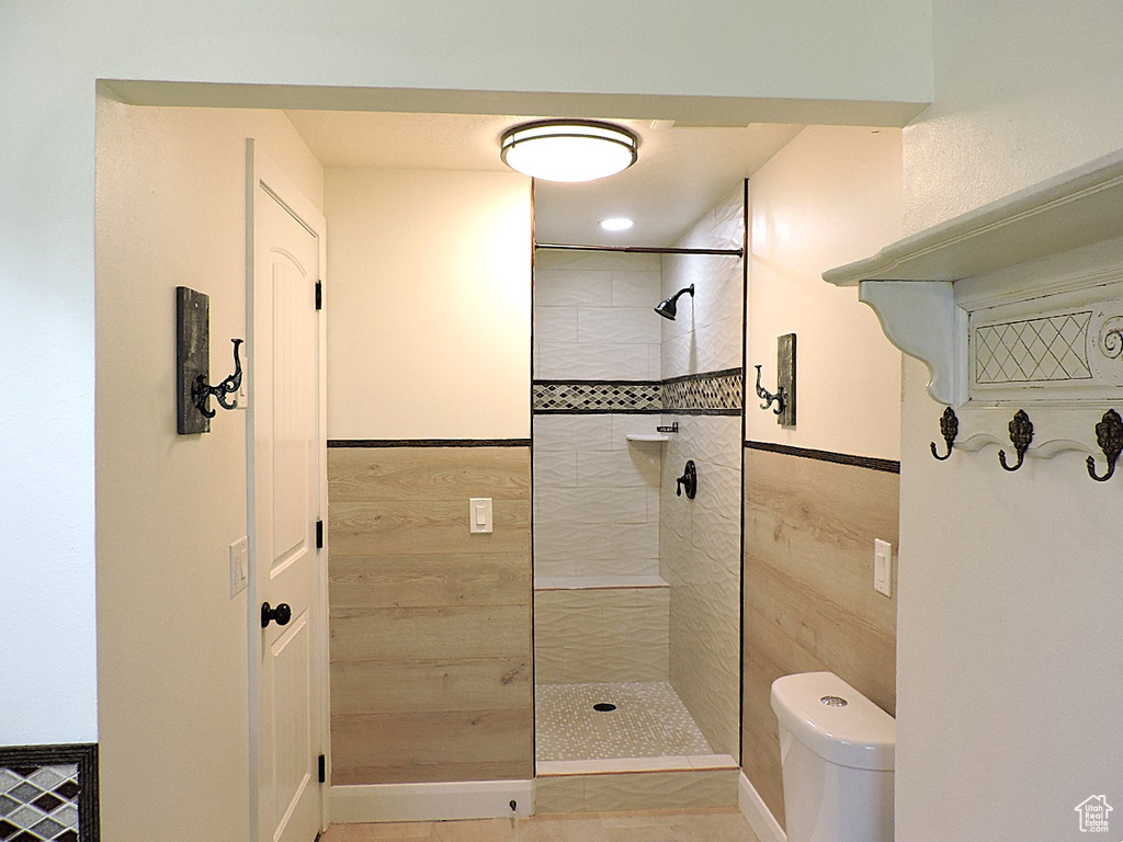 Bathroom with a wainscoted wall, a tile shower, and toilet