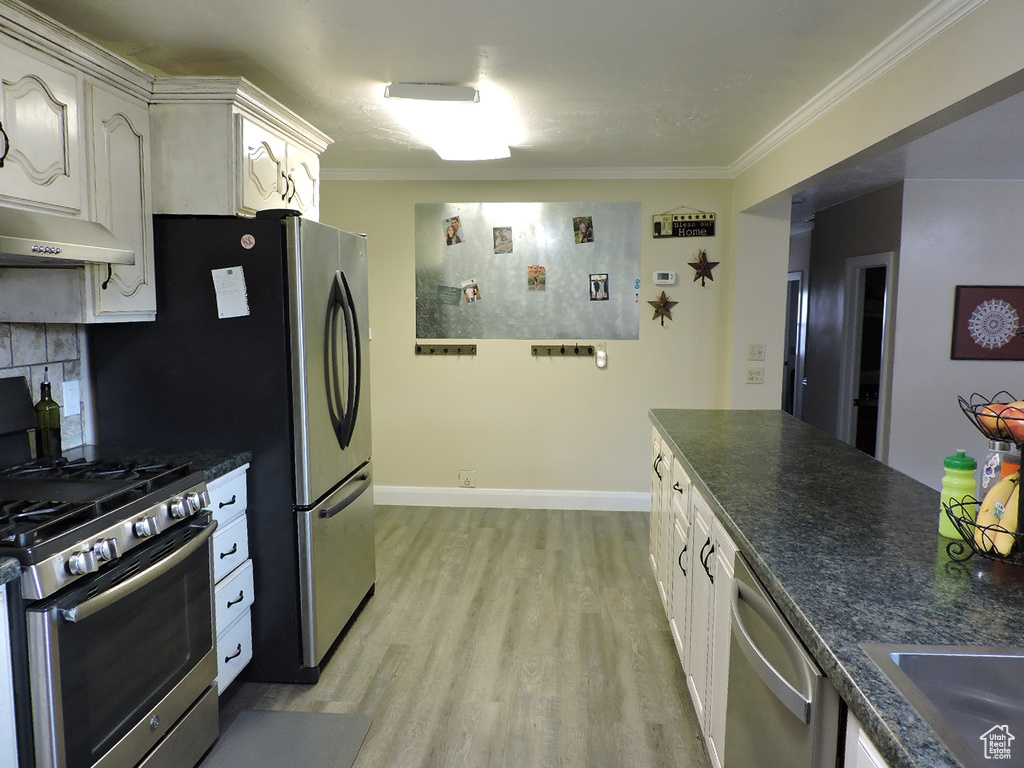 Kitchen with stainless steel appliances, white cabinets, crown molding, light hardwood / wood-style floors, and tasteful backsplash