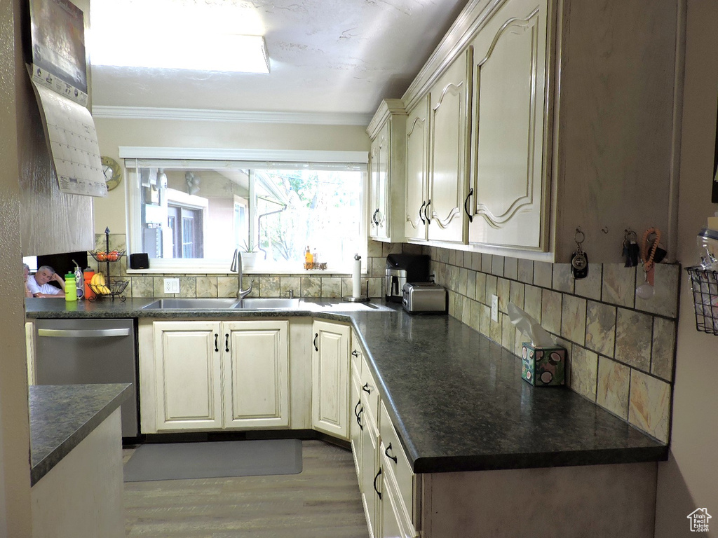 Kitchen with dishwasher, backsplash, sink, ornamental molding, and light hardwood / wood-style flooring