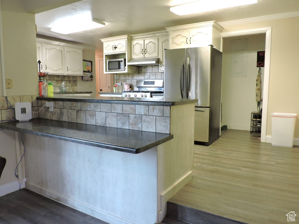 Kitchen featuring kitchen peninsula, hardwood / wood-style flooring, appliances with stainless steel finishes, and decorative backsplash