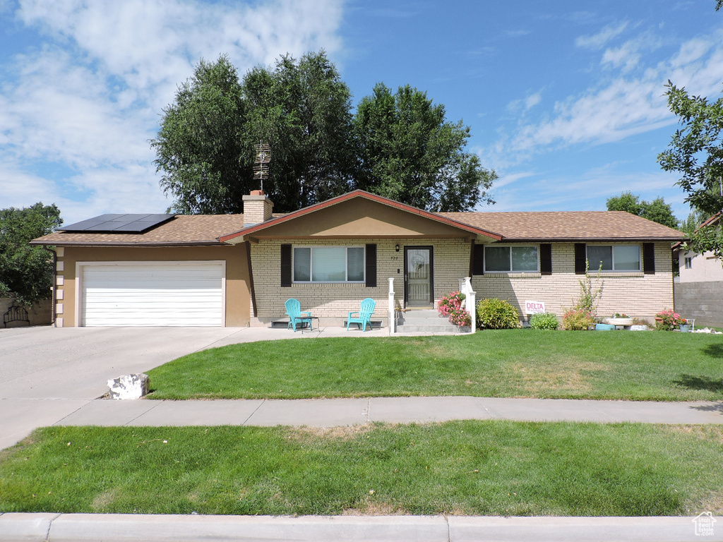 Ranch-style house with solar panels, a front yard, and a garage