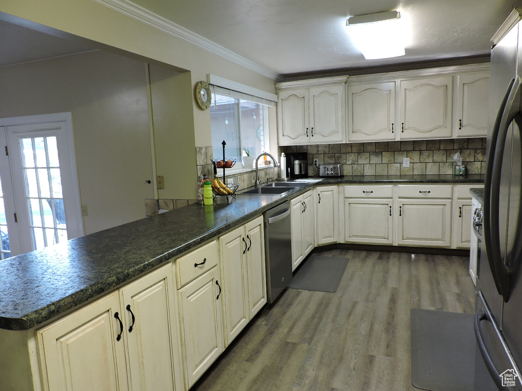 Kitchen with appliances with stainless steel finishes, kitchen peninsula, crown molding, hardwood / wood-style flooring, and tasteful backsplash