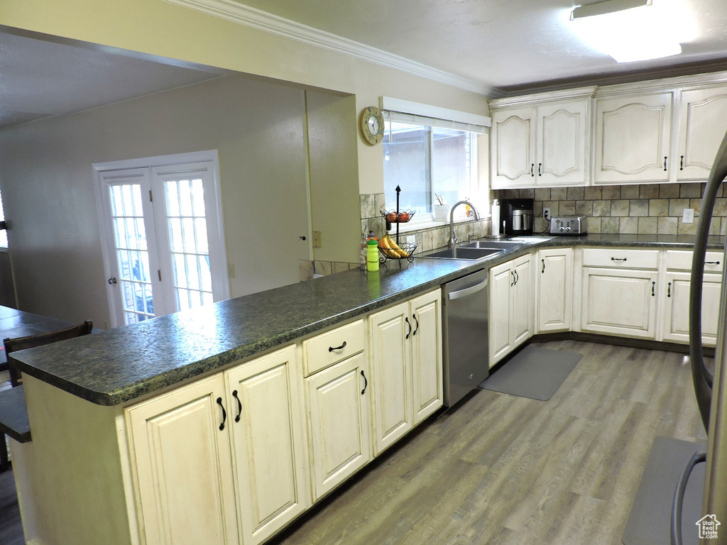 Kitchen featuring hardwood / wood-style flooring, stainless steel dishwasher, ornamental molding, tasteful backsplash, and sink