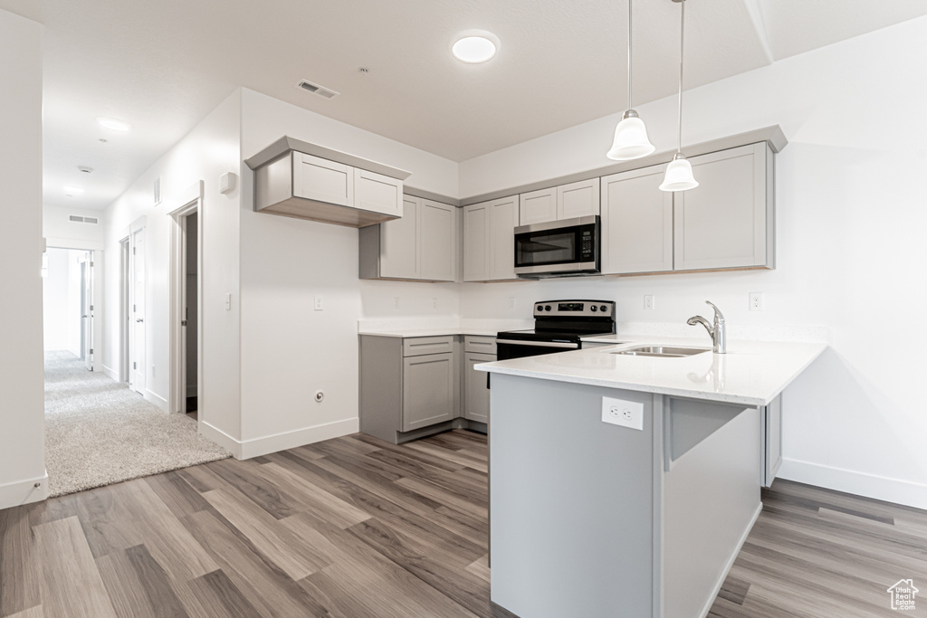 Kitchen with appliances with stainless steel finishes, sink, light hardwood / wood-style flooring, decorative light fixtures, and gray cabinets