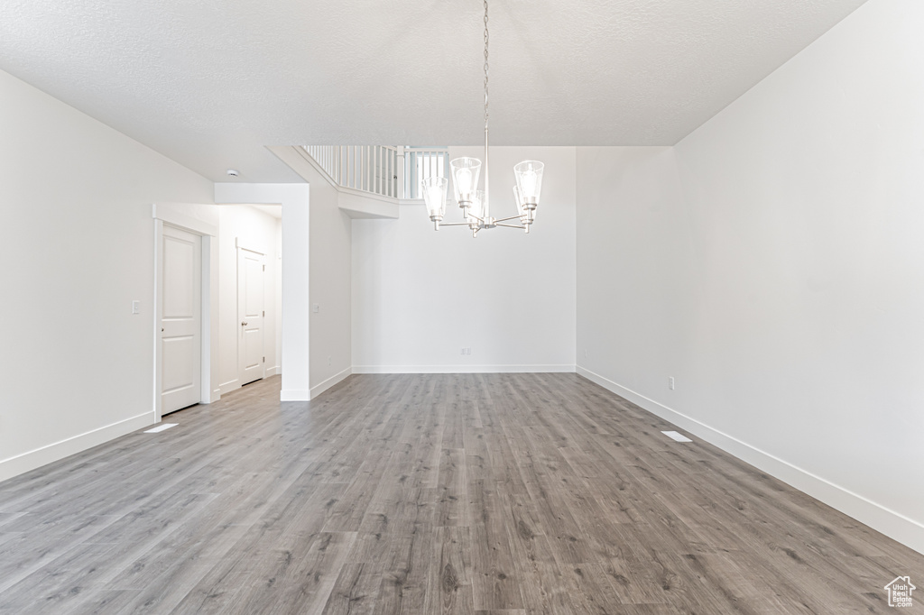 Spare room with a notable chandelier, a textured ceiling, baseboards, and wood finished floors