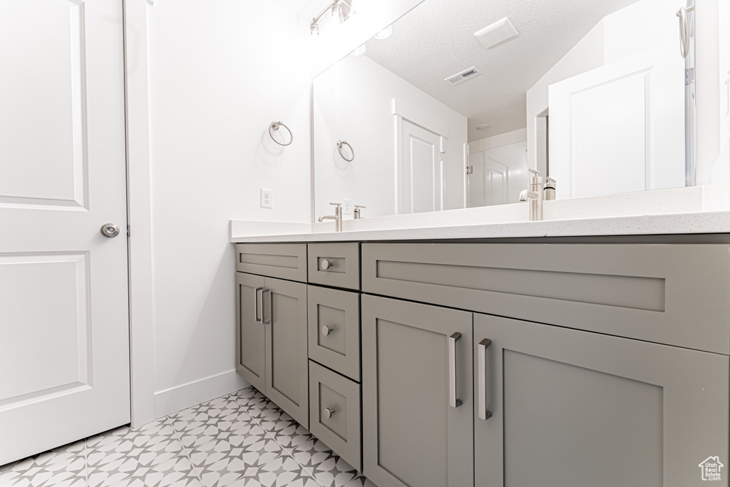 Bathroom with a textured ceiling, visible vents, baseboards, double vanity, and tile patterned floors
