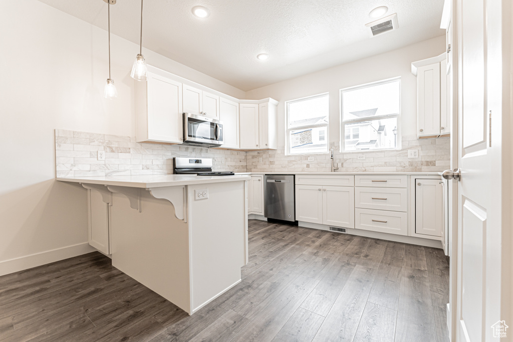 Kitchen with wood finished floors, a peninsula, stainless steel appliances, visible vents, and decorative backsplash