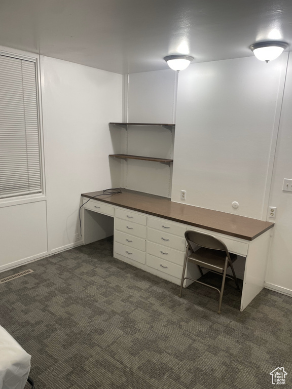 Unfurnished office featuring dark colored carpet and built in desk