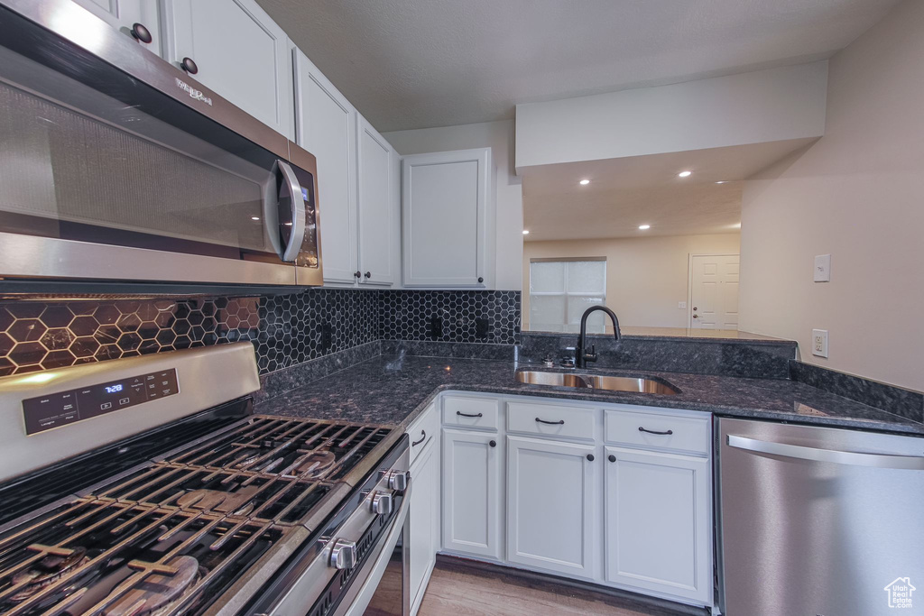 Kitchen with kitchen peninsula, dark stone counters, backsplash, stainless steel appliances, and sink