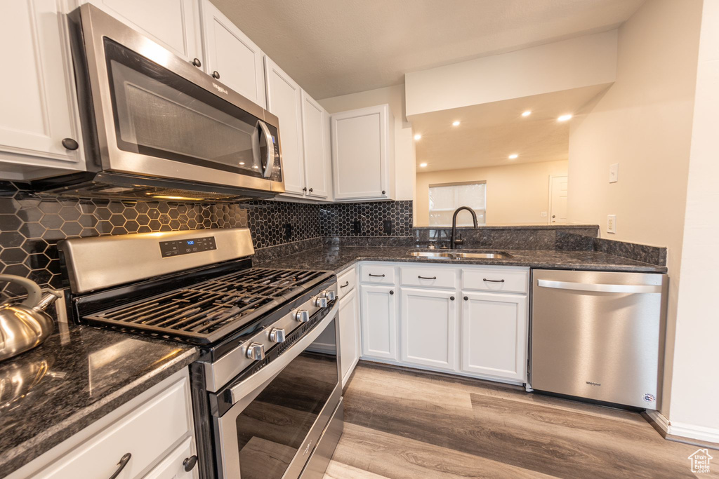 Kitchen featuring stainless steel appliances, white cabinets, sink, light hardwood / wood-style floors, and backsplash
