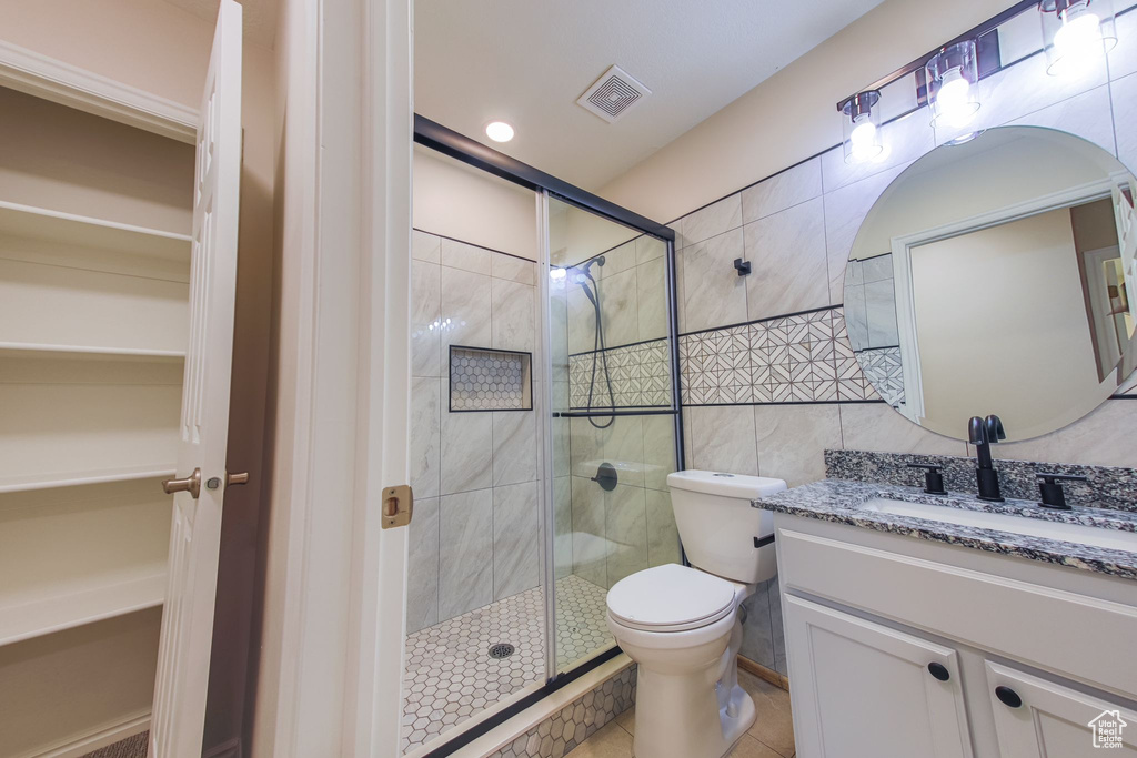 Bathroom featuring tile patterned flooring, an enclosed shower, toilet, vanity, and tile walls