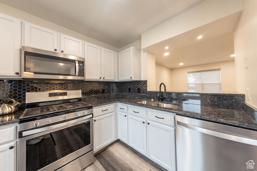 Kitchen featuring light wood-type flooring, white cabinets, appliances with stainless steel finishes, decorative backsplash, and sink