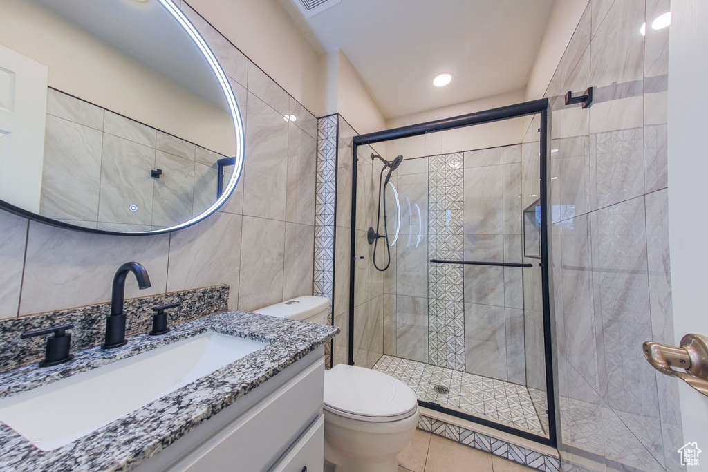 Bathroom with a shower with door, tile walls, tile patterned floors, toilet, and vanity