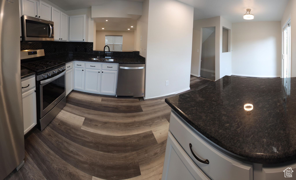 Kitchen with appliances with stainless steel finishes, wood-type flooring, white cabinets, and sink